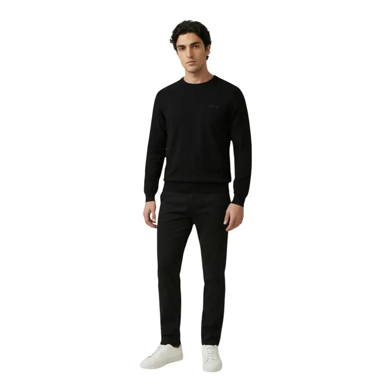 Antony Morato Schwarzer Herren-Strickpullover aus Baumwolle mit langen Ärmeln und Rundhalsausschnitt sowie dezentem Logo, kombiniert mit schwarzer Hose und weißen Sneakers.