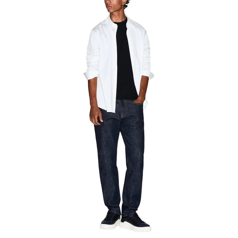 A man wearing an Armani Exchange men black cotton t shirt paired with a white shirt, dark blue jeans, and black sneakers