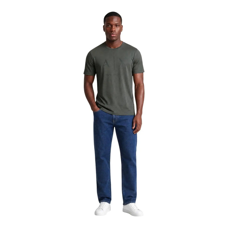 A man wearing an Armani Exchange men green cotton t shirt with black graphic detailing paired with blue jeans and white sneakers
