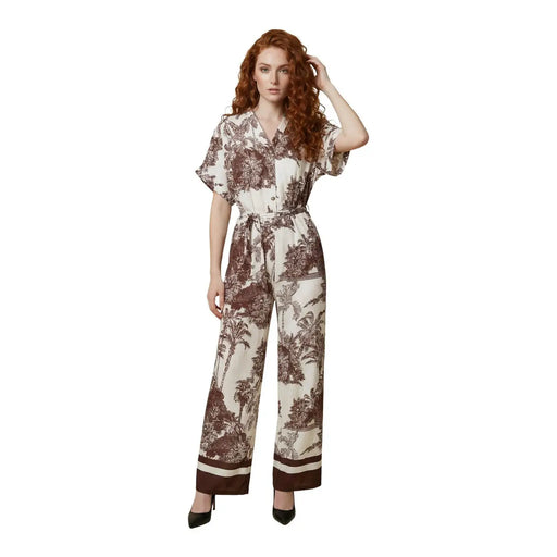 Eine Frau trägt einen beigefarbenen Artigli-Jumpsuit aus Viskose mit V-Ausschnitt, braunem Pflanzenmuster und passendem Taillengürtel.