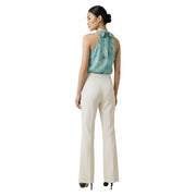 A woman wearing Artigli women trousers white zip front pockets in cream with a teal silk halter top with a bow at the back