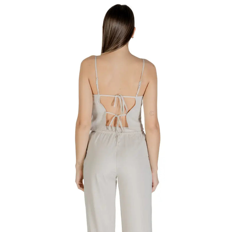 A light gray satin jumpsuit with thin straps and back tie detail complementing a beige sleeveless round neck polyester top