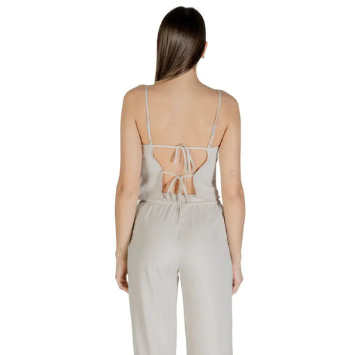 A light gray satin jumpsuit with thin straps and back tie detail complementing a beige sleeveless round neck polyester top