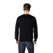 Male model wearing a black long-sleeved sweater paired with dark wash jeans