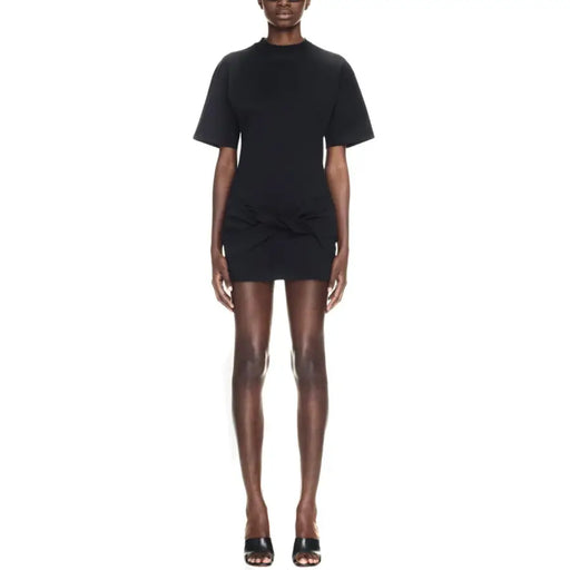Black short-sleeved mini dress with high neckline and gathered waist detail paired with sculptural heels