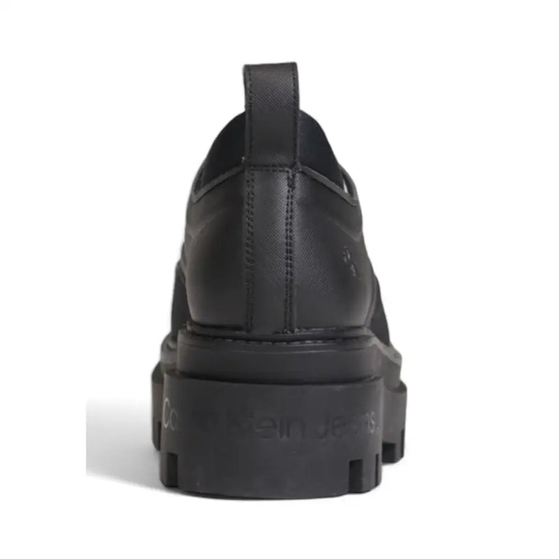 Calvin Klein black leather slip-on women’s shoe with chunky rubber sole and embossed logo on heel back side view