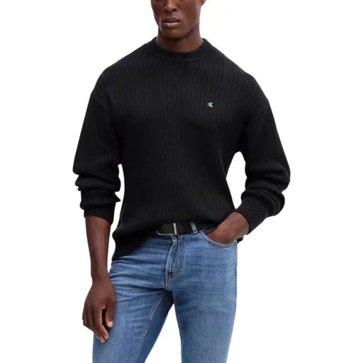 Black ribbed crew neck sweater with a small embroidered logo on the chest.