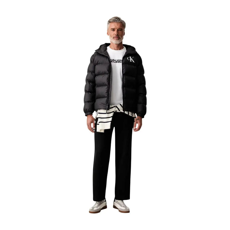 Black quilted puffer jacket with hood and white calvin klein logo on chest for men with black cotton trousers