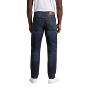 Dark indigo cotton denim jeans with classic five-pocket design and brown leather brand patch on waistband by Calvin Klein Jeans