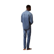 Un homme portant un jean Calvin Klein bleu en coton, coupe slim, et une chemise en jean délavée assortie.