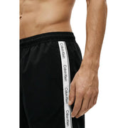Black Calvin Klein Jeans men swimwear athletic pants with white vertical stripe and repeating Calvin Klein branding