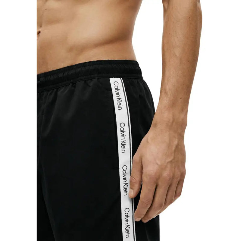 Black Calvin Klein Jeans men swimwear athletic pants with white vertical stripe and repeating Calvin Klein branding