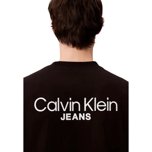 Rückansicht eines schwarzen Calvin Klein Jeans Herren-T-Shirts aus Baumwolle mit auffälligem weißen Aufdruck auf der Rückseite.