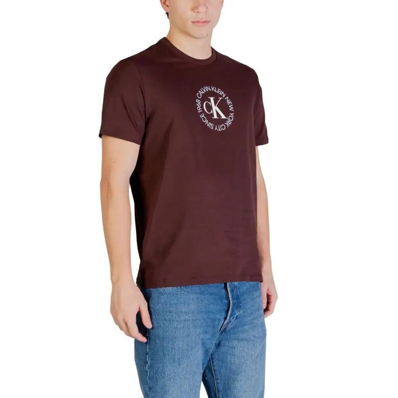 Bordeauxrotes Calvin Klein Jeans Herren-T-Shirt aus Baumwolle mit weißem, kreisförmigem CK-Monogramm-Logo und dem Aufdruck „New York since 1986“.