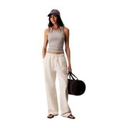 Black cylindrical duffel bag with black handles shown alongside Calvin Klein Jeans women white cotton trousers with laces