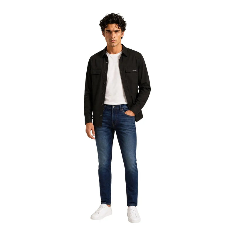 Schwarzes, langes Herrenhemd von Calvin Klein aus Baumwollmischgewebe, kombiniert mit dunkelblauen, schmal geschnittenen Jeans mit dezenten Auswaschungen an den Knien.
