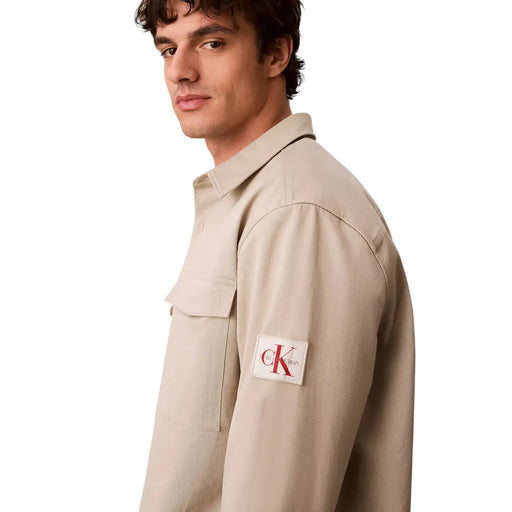Calvin Klein Chemise beige en coton à manches longues pour homme, avec poche poitrine et écusson de marque sur la manche.