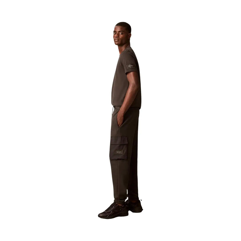 Dunkelolivgrünes Kurzarmhemd t-shirt mit dezentem Logo-Patch am linken Ärmel, kombiniert mit einer grauen Baumwollmischhose von Calvin Klein