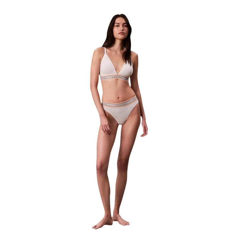 A woman wearing a white lightly lined triangle cotton bikini set with elastic calvin klein logo straps