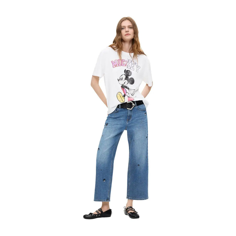 Weißes T-Shirt mit Mickey-Mouse-Motiv, pinkfarbener Schrift und schwarz-gelber Illustration, kombiniert mit einer blauen Baumwolljeans von Desigual für Damen.