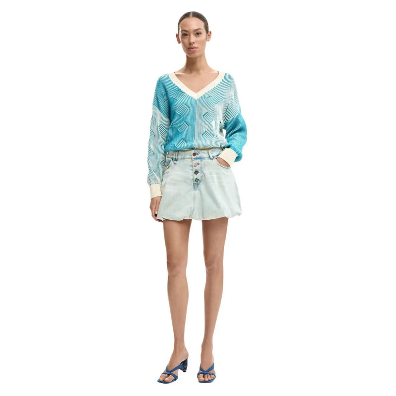 A woman wearing a turquoise and cream patterned knit sweater with long sleeves paired with a light blue Desigual cotton denim skirt