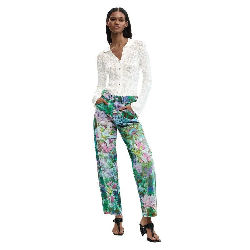 Frau trägt hellblaue Desigual-Damenjeans aus Baumwolle mit auffälligem Blumenmuster und weitem Bein sowie ein weißes Spitzenhemd