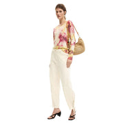 Woven straw shoulder bag with natural textured surface and gold tone strap paired with desigual beige cotton trousers