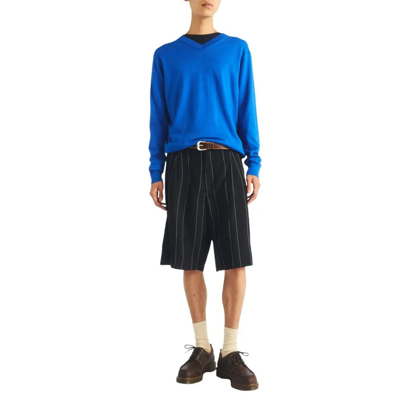Ein leuchtend blauer, langärmeliger V-Ausschnitt-Pullover wird über einem schwarzen Unterhemd getragen und mit braunen Dr. Martens Herren-Lederstiefeln zum Hineinschlüpfen kombiniert.