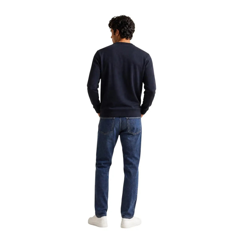 Ein Mann trägt ein schwarzes ea7 Herren-Baumwoll-Sweatshirt in regulärer Passform mit marineblauen langen Ärmeln und dunkelblauen Jeans.