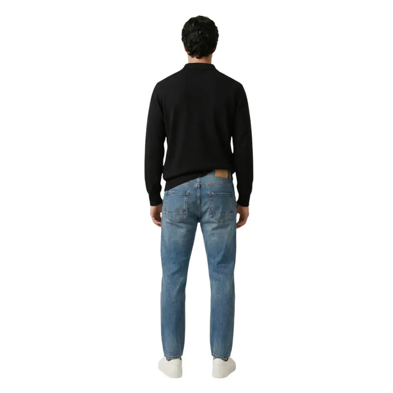 Un jean en denim bleu moyen avec un écusson de marque en cuir marron sur la ceinture arrière. gianni lupo