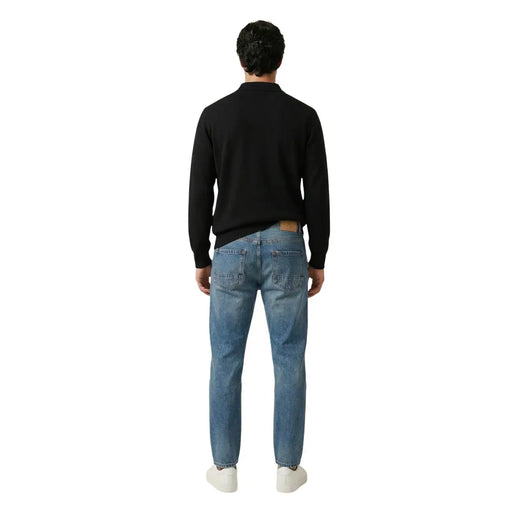 A pair of medium-wash blue denim jeans with a brown leather brand patch on the back waistband by gianni lupo