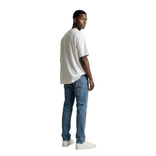 A man wearing a gianni lupo white round neck t shirt made of 100% cotton paired with medium-wash blue jeans