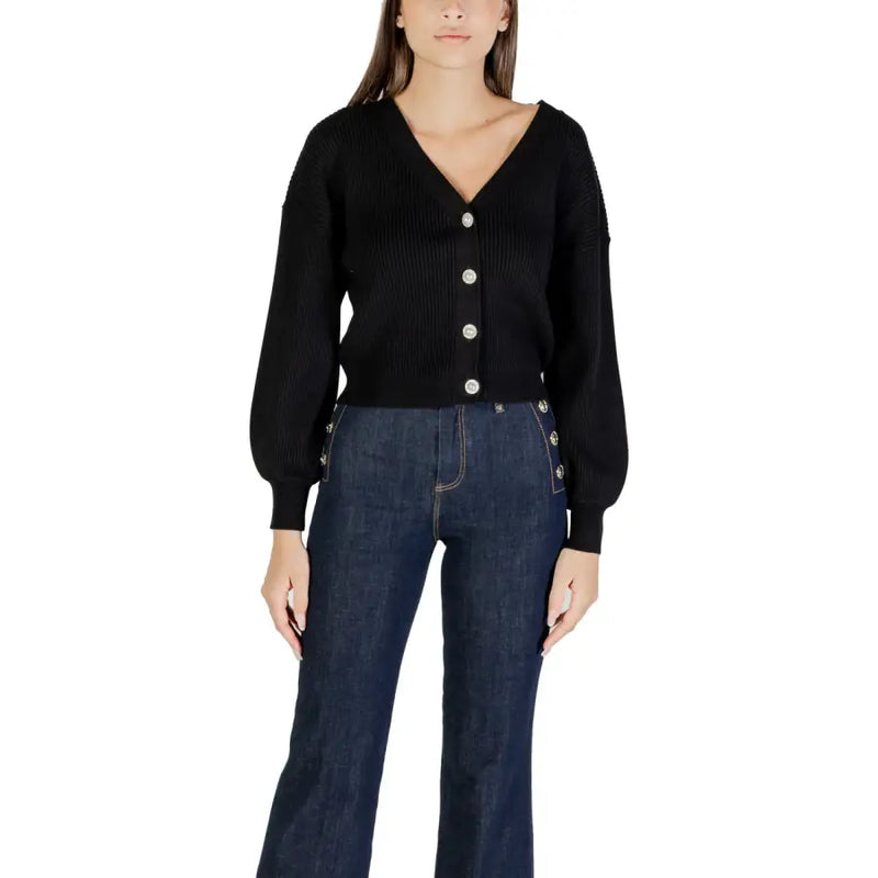 Woman wearing black ribbed knit cardigan with silver buttons and dark wide-leg jeans