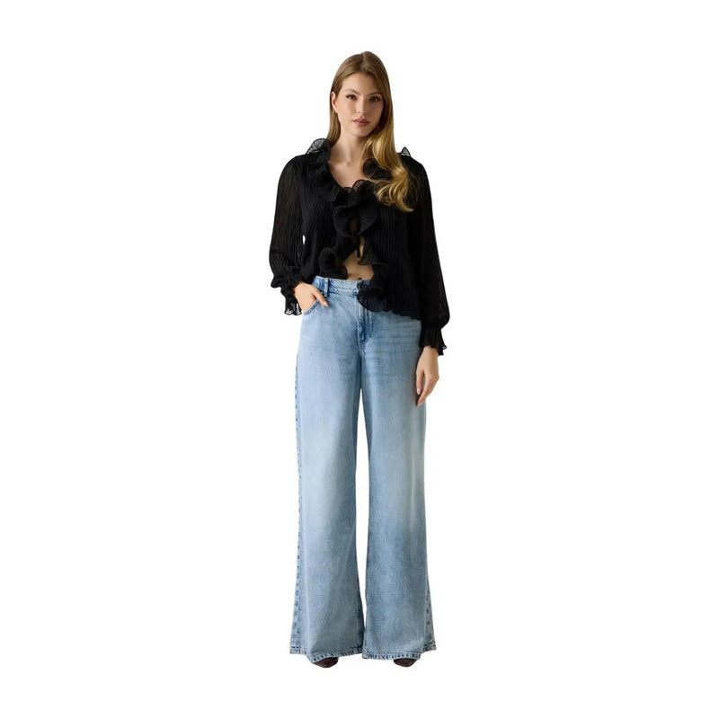 A woman wearing Guess women wide loose lyocell blend blue jeans paired with a black ruffled blouse with sheer sleeves
