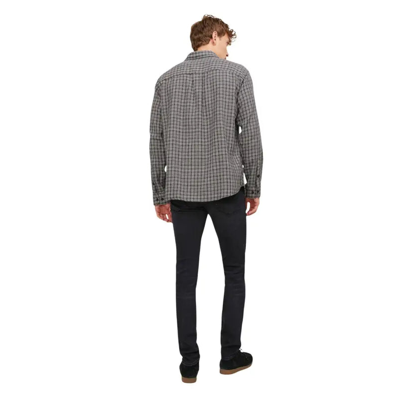 Ein Mann, der ein schwarz-weiß kariertes Langarmhemd mit Knopfleiste und schwarze Herrenjeans von Jack & Jones trägt.