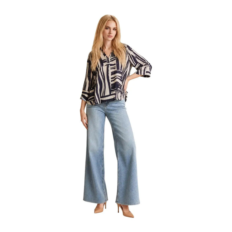 A woman wears a Jacqueline de Yong blue viscose v neck top with 3 4 sleeves paired with light denim flare pants