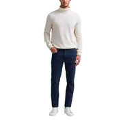 Man wearing cream turtleneck sweater and dark blue trousers with white sneakers