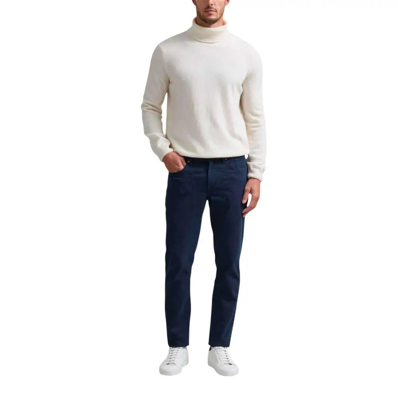 Man wearing cream turtleneck sweater and dark blue trousers with white sneakers