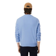 Hellblauer Lacoste Herren-Strickpullover aus Wolle mit Rundhalsausschnitt, gerippten Bündchen und Saum, kombiniert mit einer hellbraunen Cordmütze.