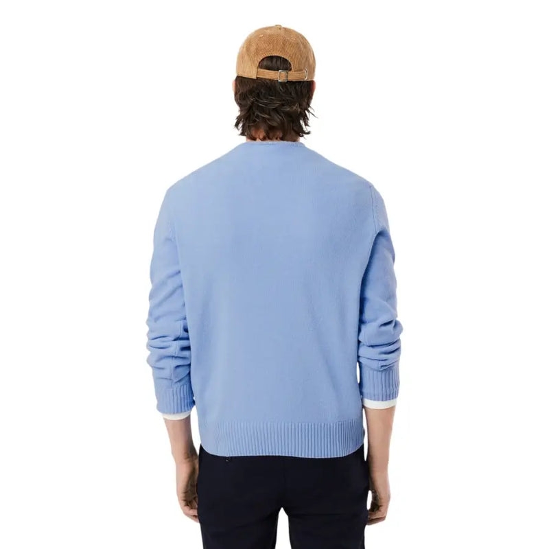 Hellblauer Lacoste Herren-Strickpullover aus Wolle mit Rundhalsausschnitt, gerippten Bündchen und Saum, kombiniert mit einer hellbraunen Cordmütze.