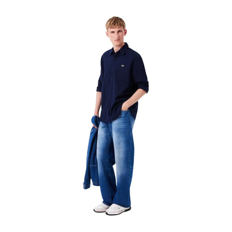 Marineblaues Button-Down-Hemd mit kleinem, gesticktem Logo auf der Brust, kombiniert mit weißen Lacoste-Sneakers aus Wildleder-Nylon für Herren.