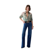 Eine Frau trägt eine blaue Baumwoll-Stretchjeans von Liu Jo mit weitem Bein und einen schwarzen Gürtel mit goldener Logoschnalle.