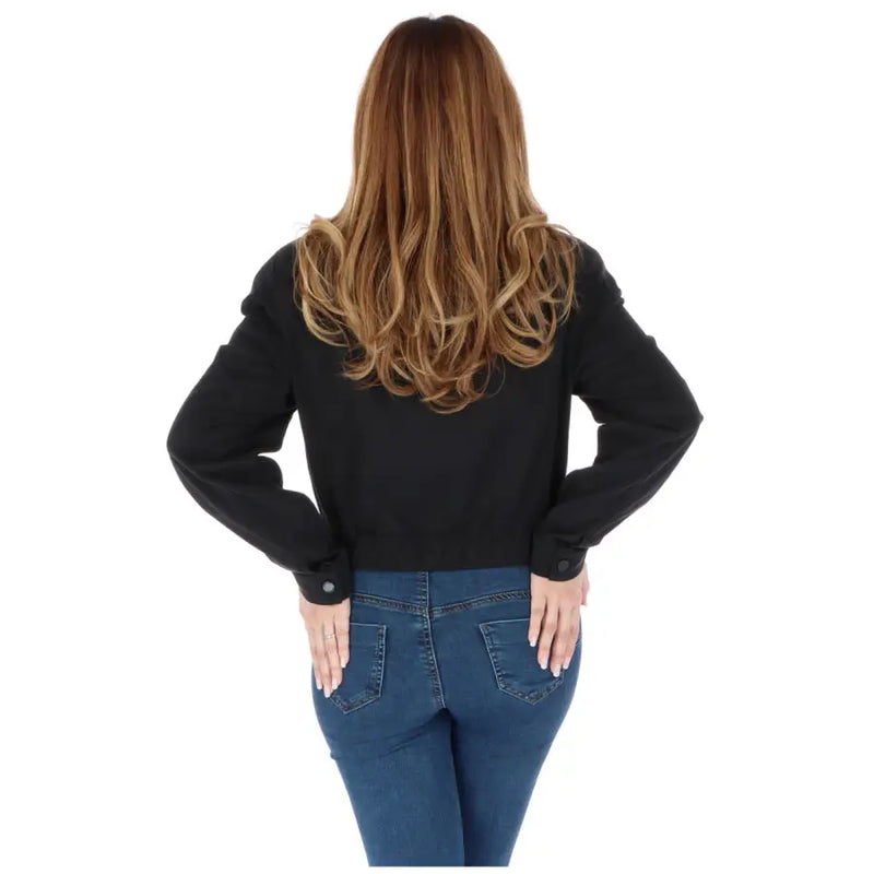 Woman with long wavy brown hair wearing a black blazer and blue jeans from behind