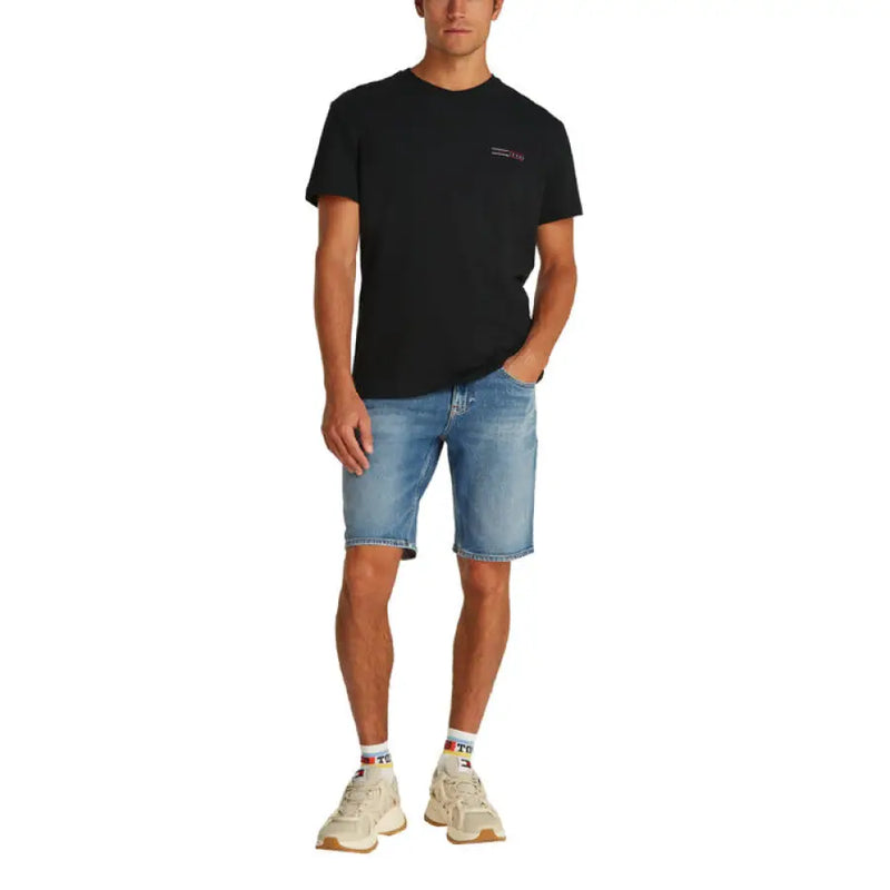 Male model in a black crewneck T shirt and denim shorts showcasing casual style