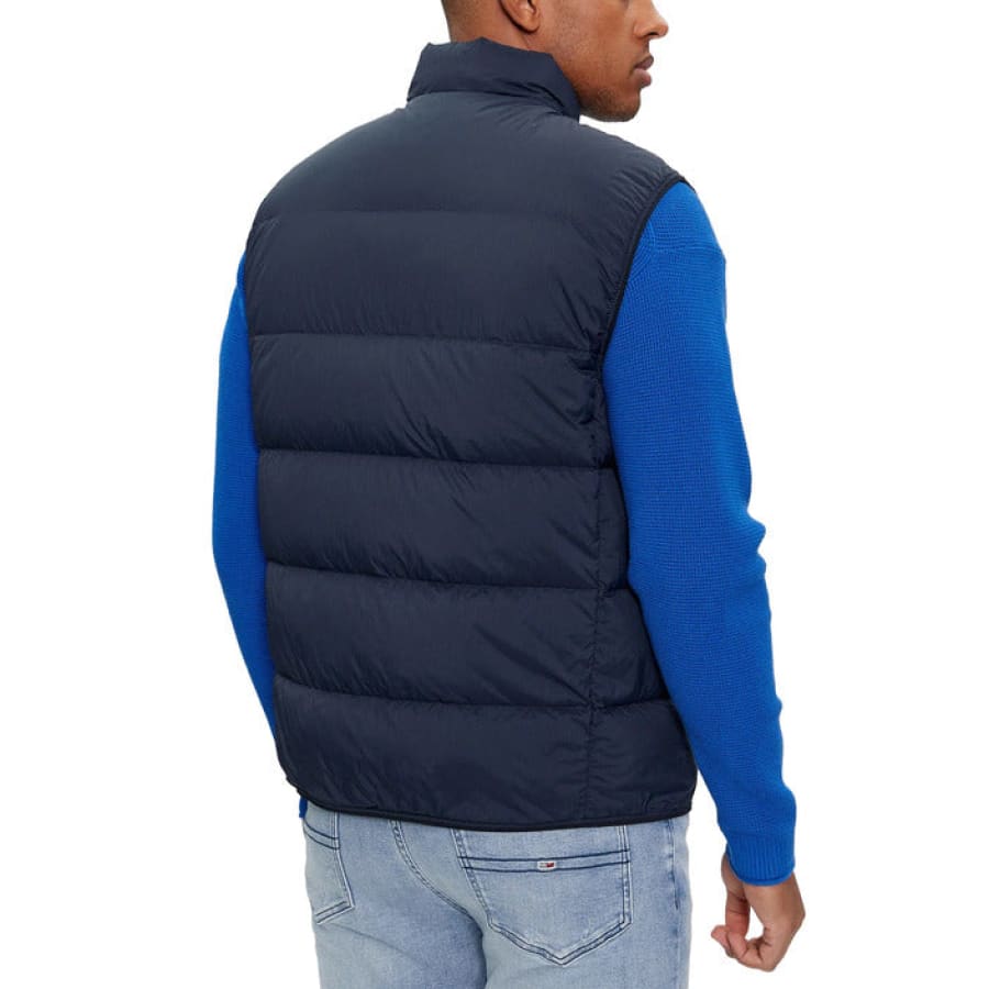 Man wearing Tommy Hilfiger Jeans Men Jacket in blue sweater and black vest looking back.