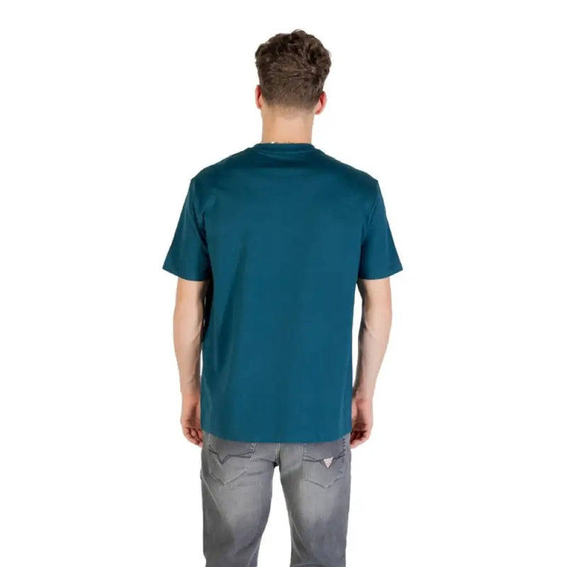 Man wearing a teal crew neck T shirt and gray jeans, showcasing men’s casual fashion