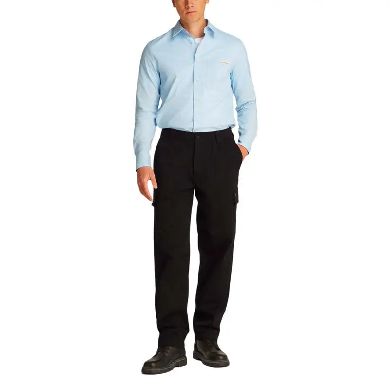 A man wearing men’s black cargo pants by Calvin Klein paired with a light blue long-sleeved button-up shirt