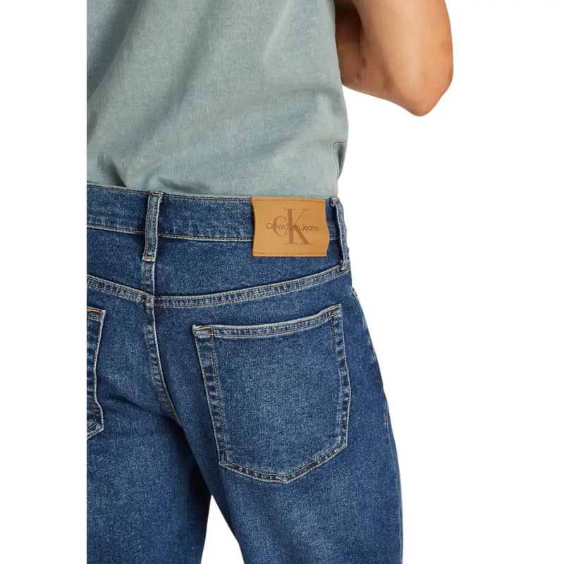 Mens blue denim shorts with tan leather calvin klein jeans logo patch on the back waistband