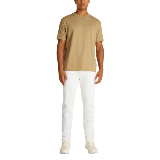 Men’s white denim jeans paired with a beige short-sleeved crew neck t-shirt featuring a small white embroidered logo