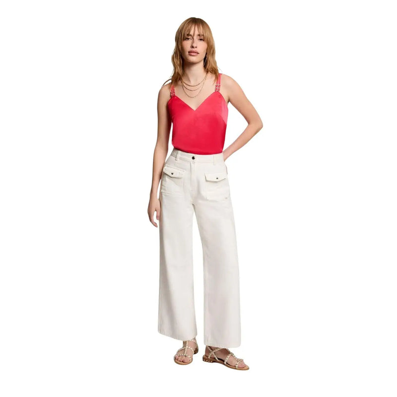 A woman wears a Morgan De Toi women coral v neck satin camisole with thin straps paired with white wide-leg trousers